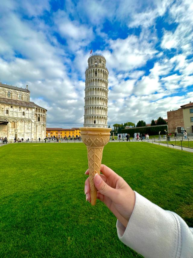 Hand holding a large ice cream cone against the backdrop of the iconic Leaning Tower of Pisa, Italy