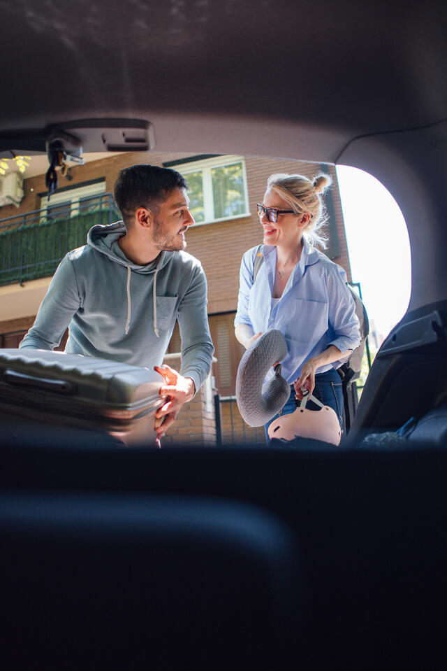 Happy Couple Putting Bags and a Suitcase in the Car Ready to Go on a Trip