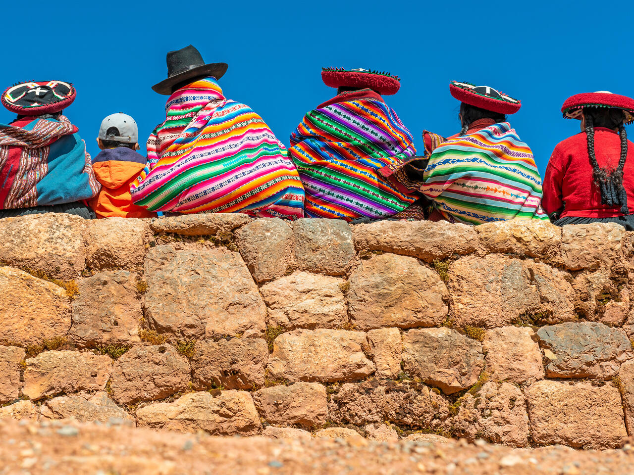A group of Quechua indigenous women in traditional clothing and a young boy sitting and chatting on an ancient Inca wall in the archaeological site of Chinchero in the region of Cusco city, Peru.